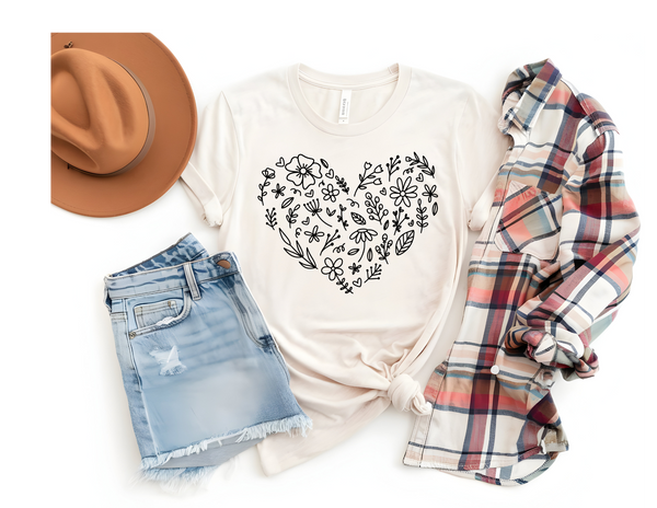 A flat lay of a cream t-shirt with a floral heart design, denim shorts, a plaid shirt, and a brown hat